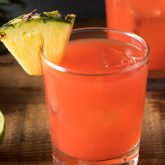Bright rum punch with fruit garnish held up against a sunlit festival stage, capturing Sugar Cane’s tropical spirit