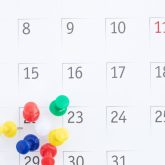 Close‑up of colourful pushpins marking dates on a calendar, representing booking a party venue in London.