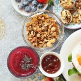 Tropical brunch spread at The Sugar Cane Bar with croissant sandwich, fresh berries, granola, chia smoothie, jam, and walnuts on a light background.