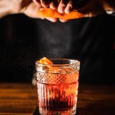 Bartender squeezing orange zest over a ruby-red tiki cocktail on a wooden bar at Sugar Cane near Battersea Power Station.