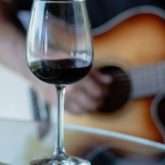 Two glasses of red wine on a table with a guitarist playing in the blurred background at Sugar Cane’s live-music cocktail bar near Wandsworth Town Station.