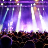 Large crowd facing a brightly lit stage with colourful spotlights during a live gig at O2 Academy Brixton.